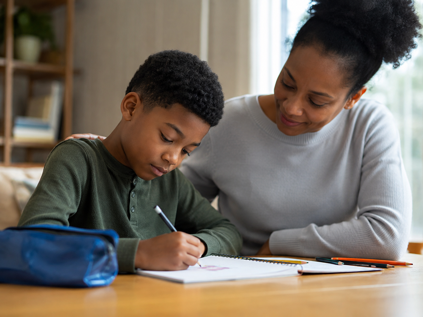 A young boy drawing in a notebook at a table.